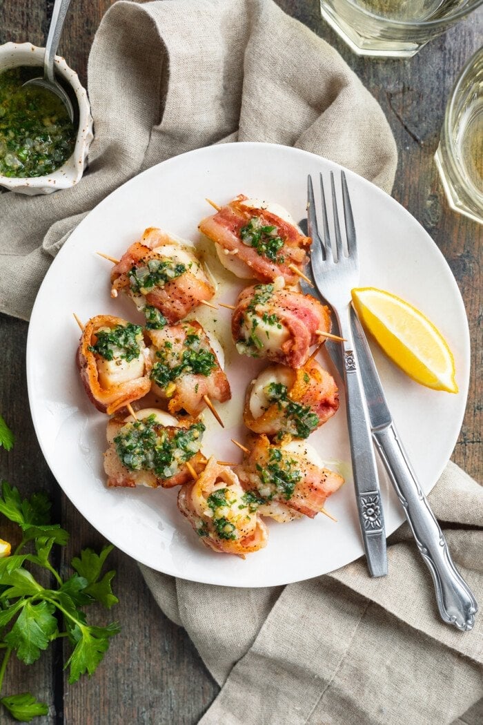 Overhead view of a plate of bacon-wrapped scallops with lemon wedges and a fork.