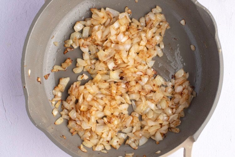 Overhead view of diced onions in a large grey skillet on a white background.
