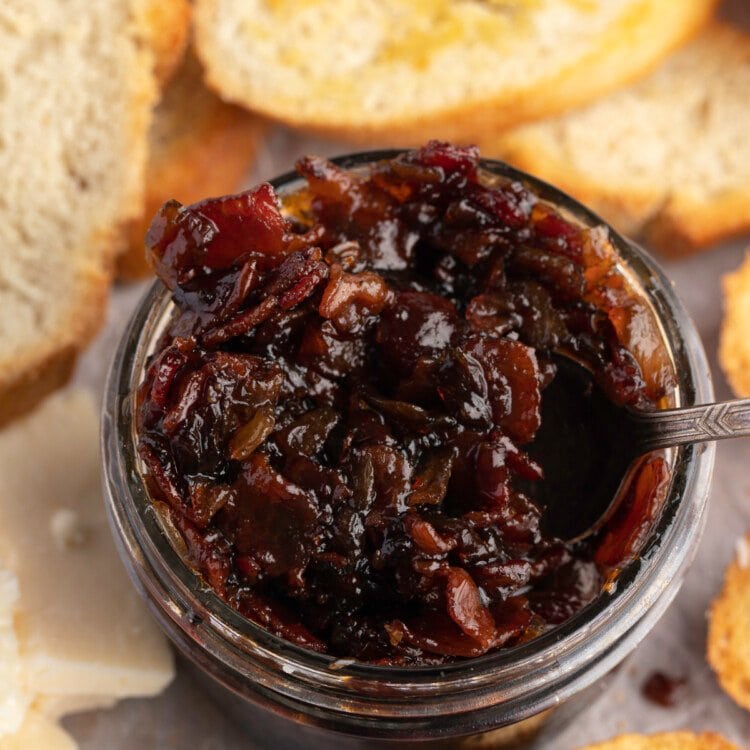 Overhead view of a jar of bacon jam surrounded by slices of crisp bread.