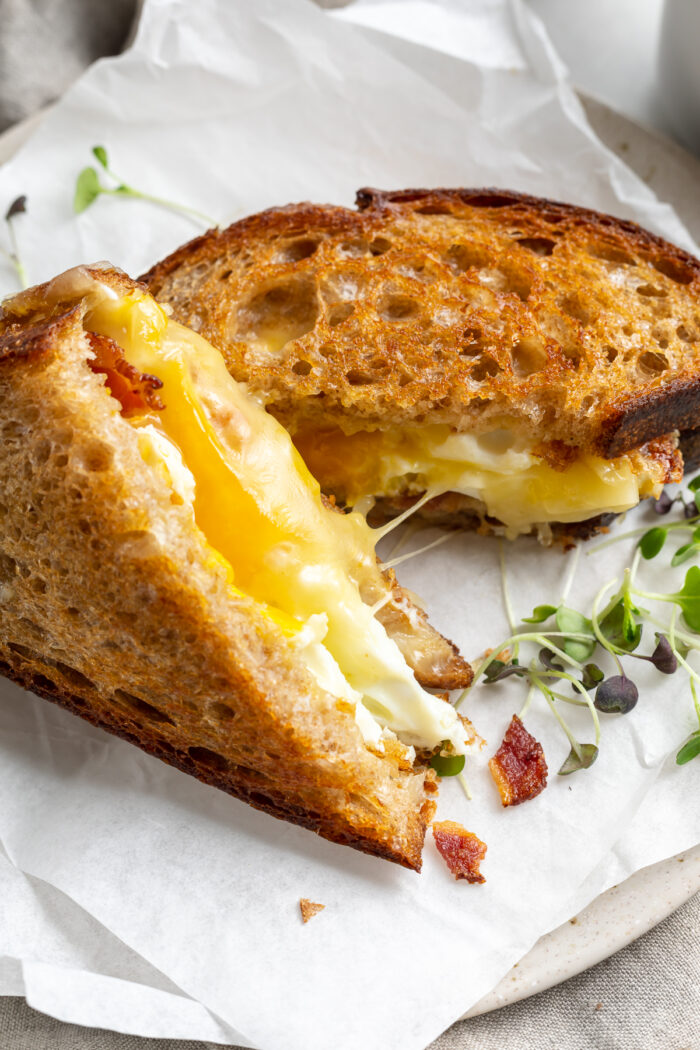A fried egg sandwich, sliced in half. One half rests on the plate while the other half stands upright to show egg and cheese.