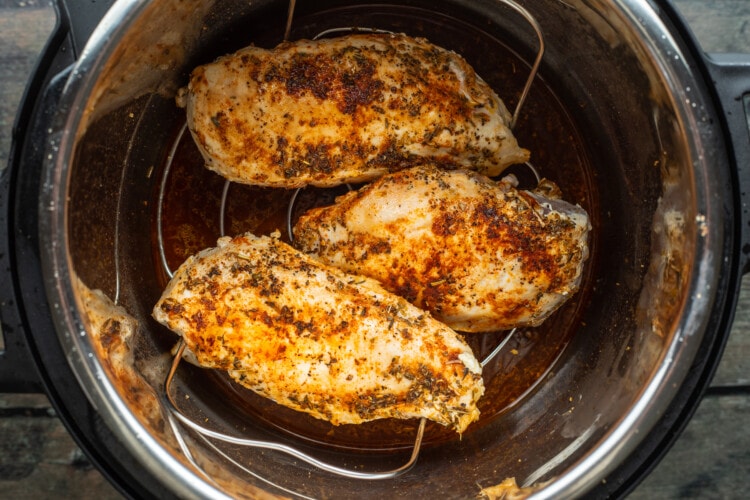 3 chicken breasts on trivet in Instant Pot over chicken broth.
