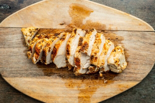 Sliced Instant Pot chicken breast on a oval wooden cutting board.