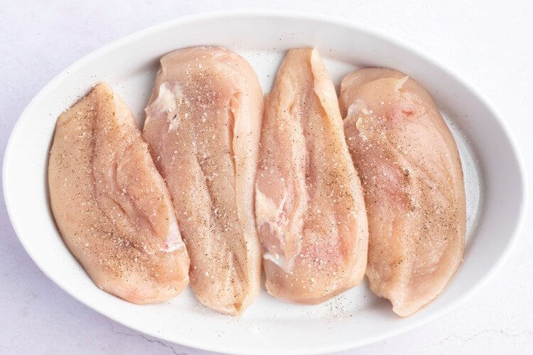 Chicken breasts in a large white oval baking dish on a white countertop.