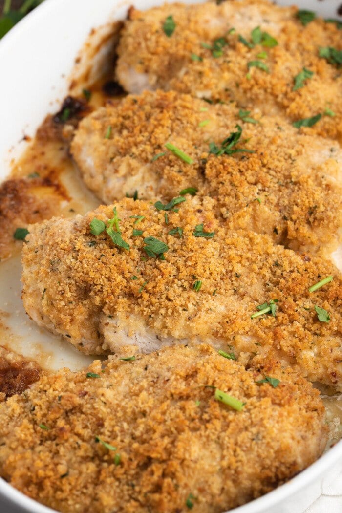 Overhead angled view of a white baking dish with 4 chicken breasts coated in breadcrumbs.