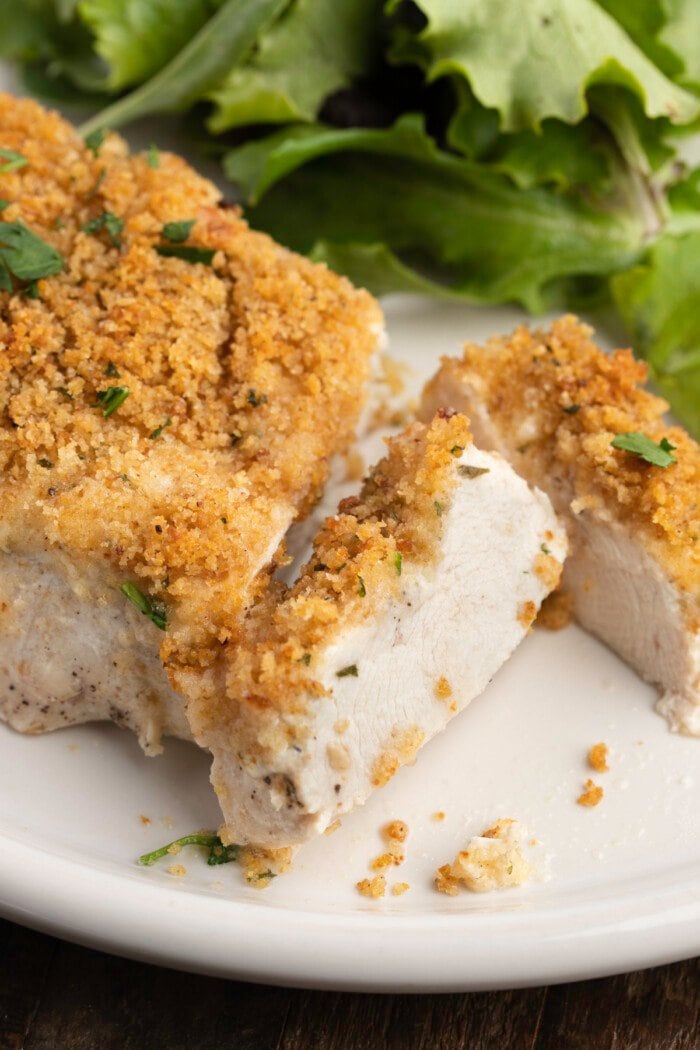 A close-up view of OMG Chicken on a plate, sliced, with a green lettuce salad in the background.