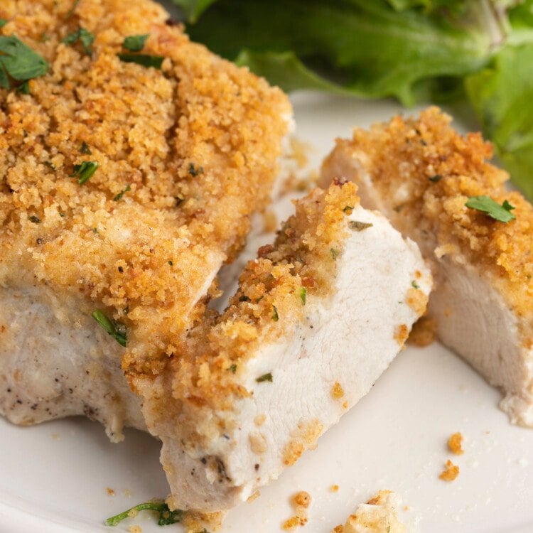 A close-up view of OMG Chicken on a plate, sliced, with a green lettuce salad in the background.