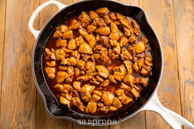 Overhead view of a large skillet with chicken thigh pieces in bourbon sauce on a wooden table.