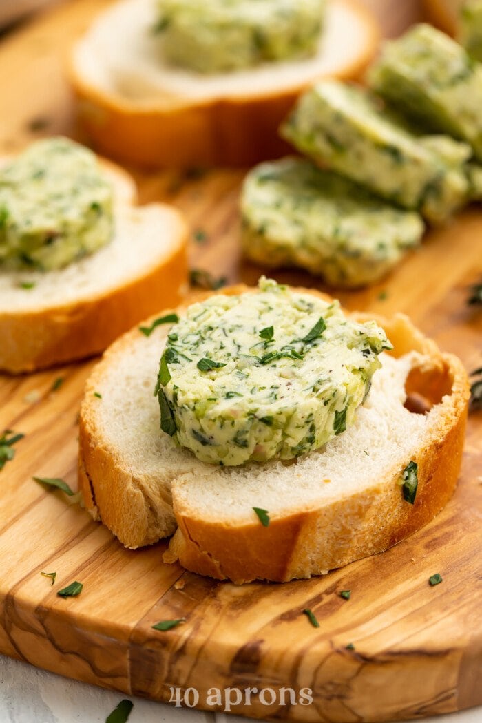 3/4-angle view of a round slice of garlic herb butter on a piece of crusty bread.