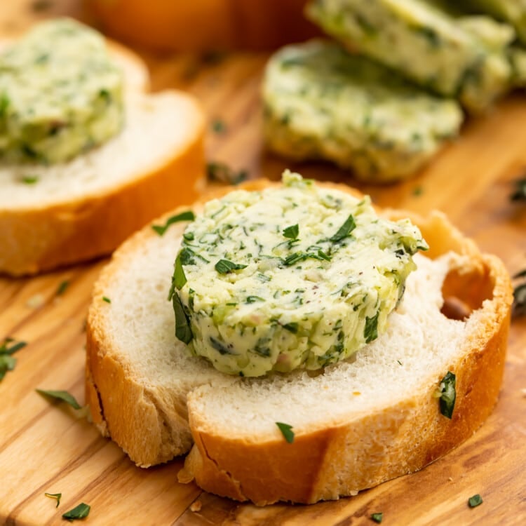3/4-angle view of a round slice of garlic herb butter on a piece of crusty bread.