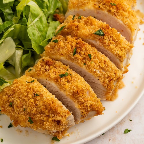 Close-up of sliced parmesan-crusted chicken breast with crispy golden breadcrumbs and fresh parsley garnish.