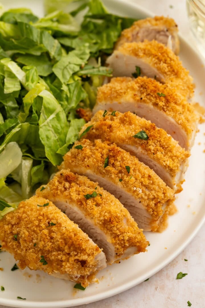 Close-up of sliced parmesan-crusted chicken breast with crispy golden breadcrumbs and fresh parsley garnish.
