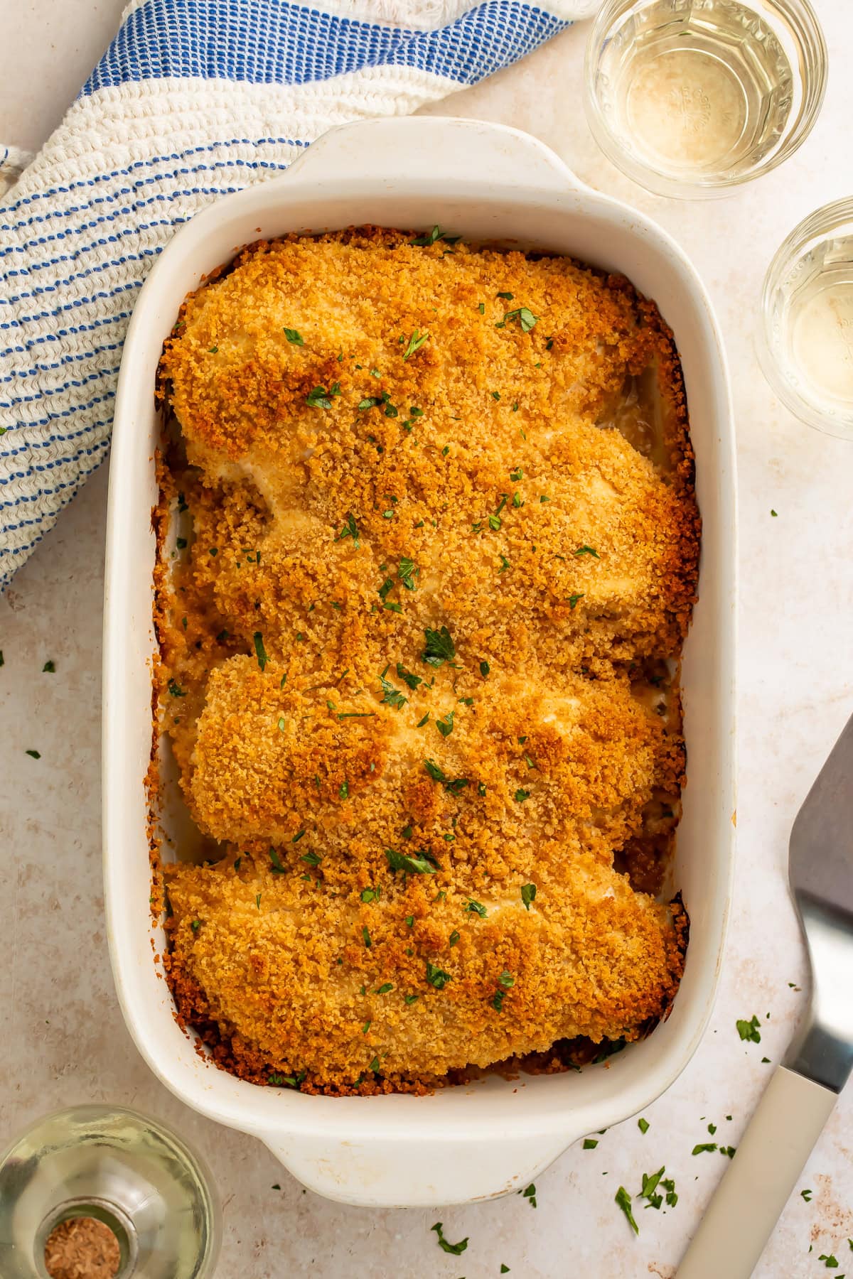 Overhead view of chicken breasts in white baking dish with golden breadcrumb topping and parsley.