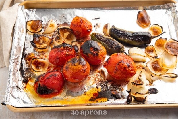 Blistered and blackened roasted vegetables on a baking sheet lined with aluminum foil.