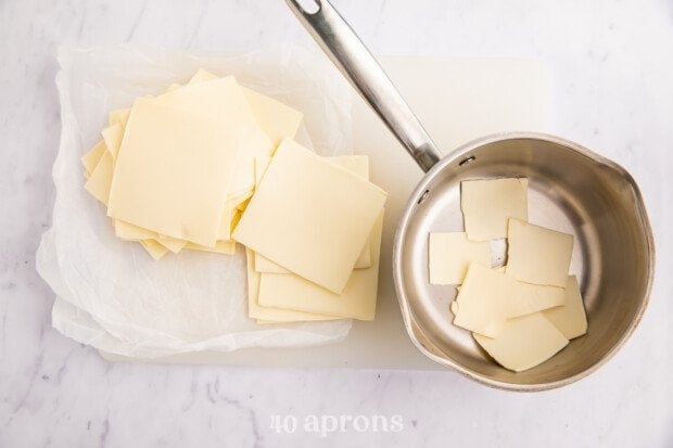 Overhead view of white American cheese on a cutting board next to a saucepan.