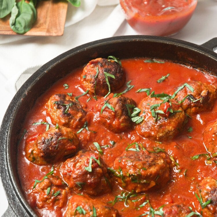 Whole30 Italian meatballs in a cast-iron skillet with marinara sauce.