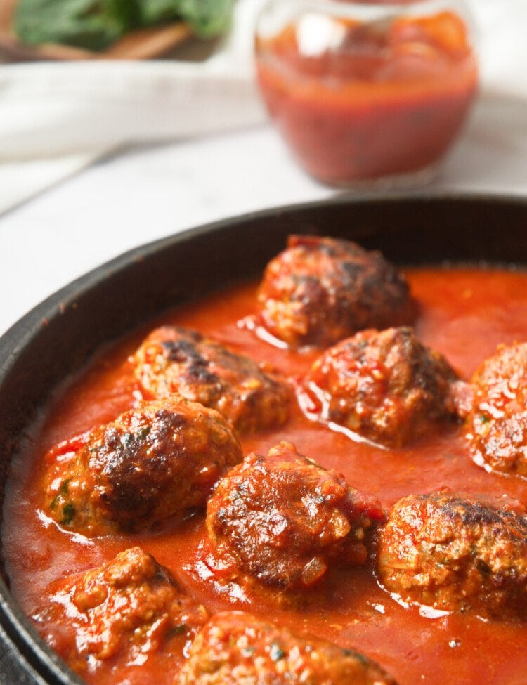 Whole30 Italian meatballs in a cast-iron skillet with marinara sauce.
