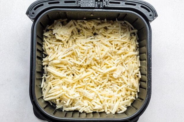 Overhead view of uncooked frozen hashbrowns in an air fryer basket.
