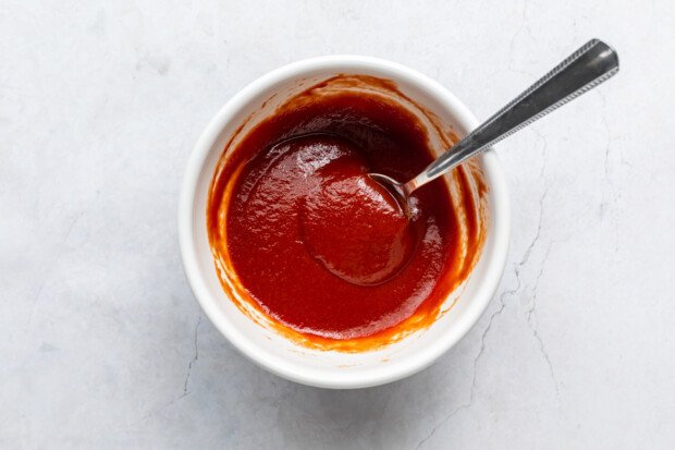 Overhead view of a small white ramekin with ketchup and chipotle adobo sauce with a spoon.