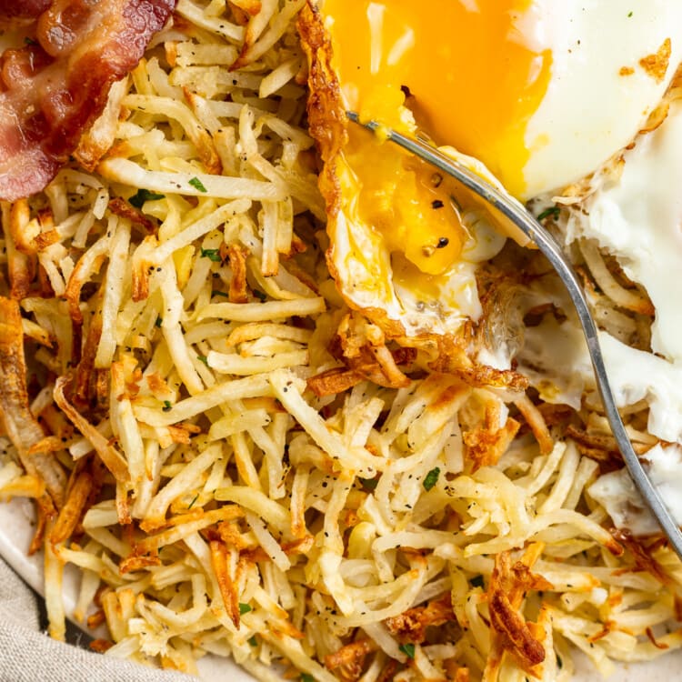 Close-up view of air fryer hashbrowns on a plate with bacon and an egg.