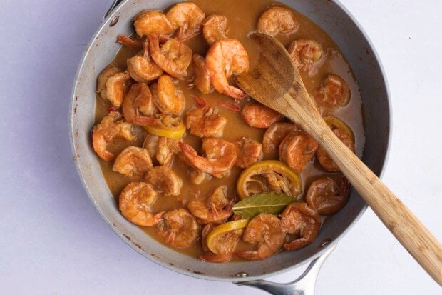 Overhead view of BBQ shrimp in a large skillet with a wooden spoon.