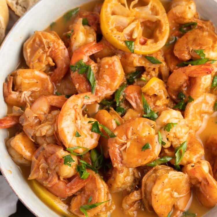 Overhead, zoomed out view of a large bowl of BBQ shrimp with crusty bread.