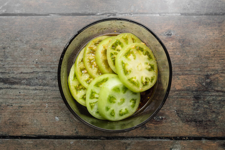 Green tomato slices in a large bowl with a balsamic marinade.