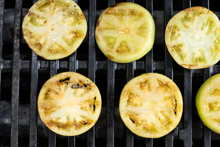 Sliced green tomatoes marinated in balsamic marinade arranged on grill grate.