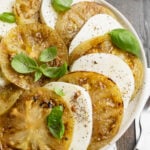 Overhead view of slices of grilled green tomatoes and fresh mozzarella arranged in a circle on plate.