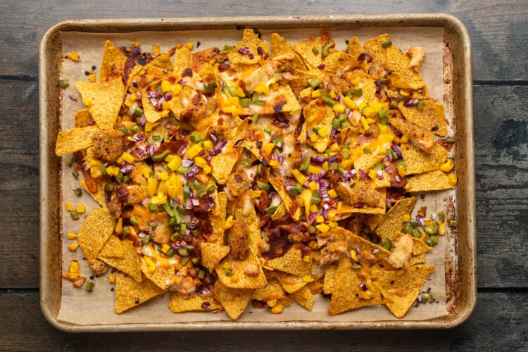 Overhead view of a baking sheet of tortilla chips, salmon, BBQ sauce, and shredded cheese.