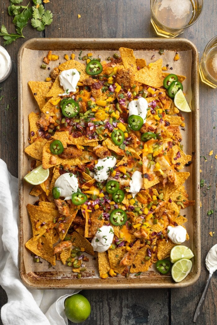Zoomed out, overhead view of a large baking sheet covered in honey chipotle salmon bbq nachos with jalapenos and dollops of sour cream.