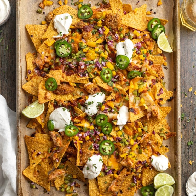 Zoomed out, overhead view of a large baking sheet covered in honey chipotle salmon bbq nachos with jalapenos and dollops of sour cream.