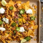 Overhead view of a large baking sheet covered in honey chipotle salmon bbq nachos with jalapenos and dollops of sour cream.