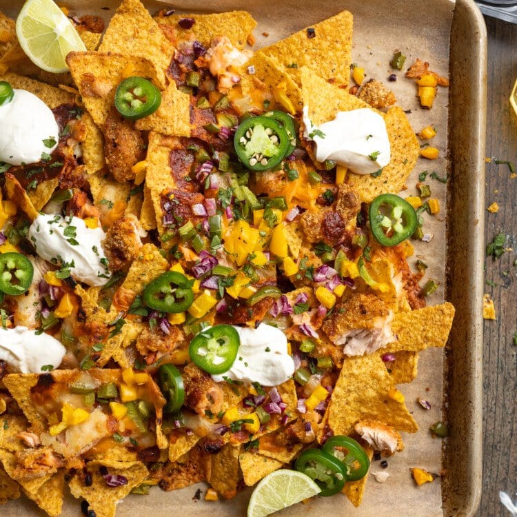 Overhead view of a large baking sheet covered in honey chipotle salmon bbq nachos with jalapenos and dollops of sour cream.