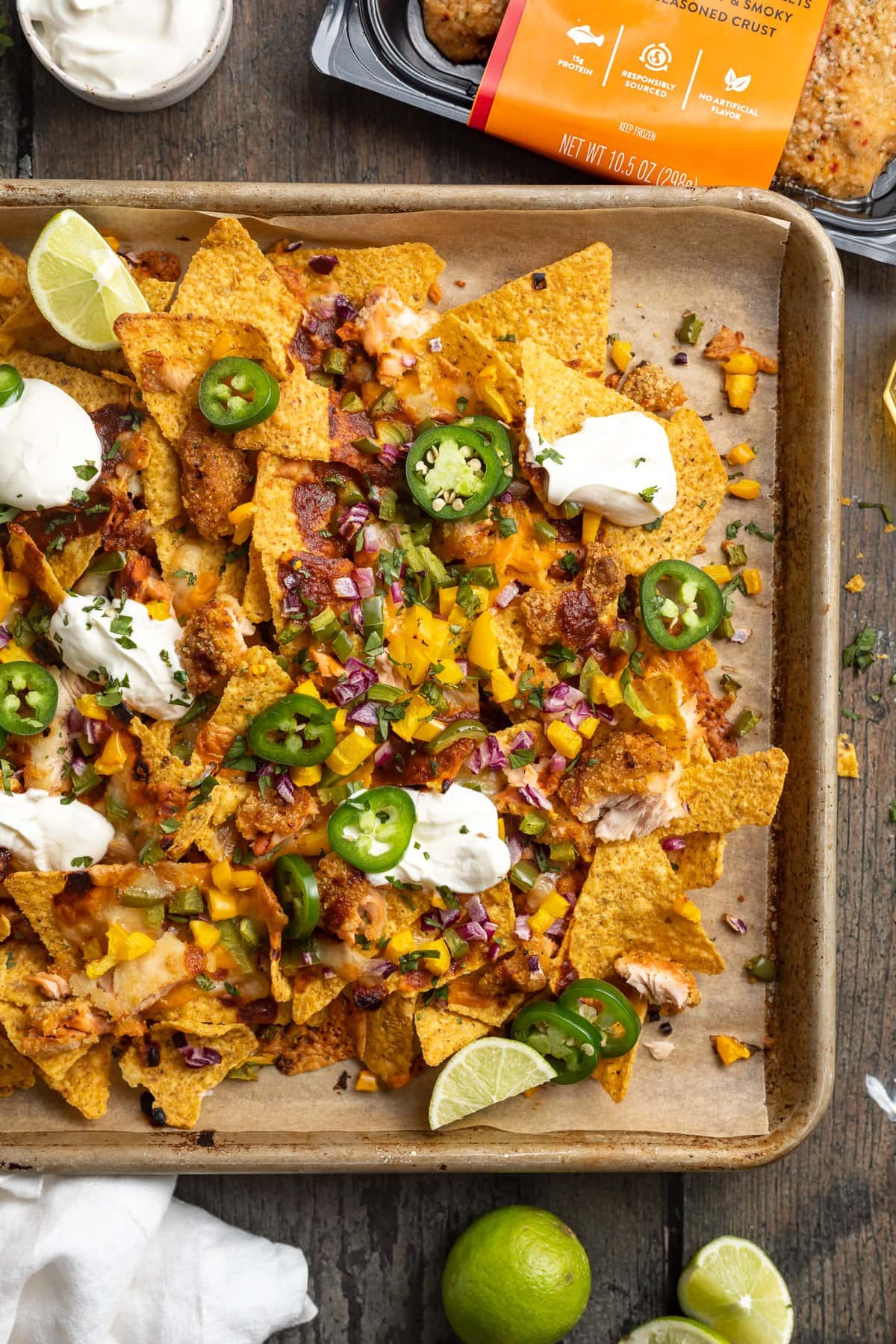 Overhead view of a large baking sheet covered in honey chipotle salmon bbq nachos with jalapenos and dollops of sour cream.