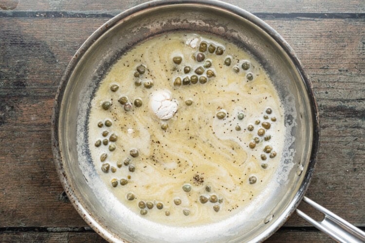 Overhead view of white wine, capers, flour, salt, and pepper in a large silver skillet.