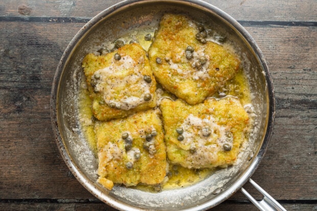 Overhead view of 4 potato-crusted cod fillets in a large skillet with a white wine sauce.