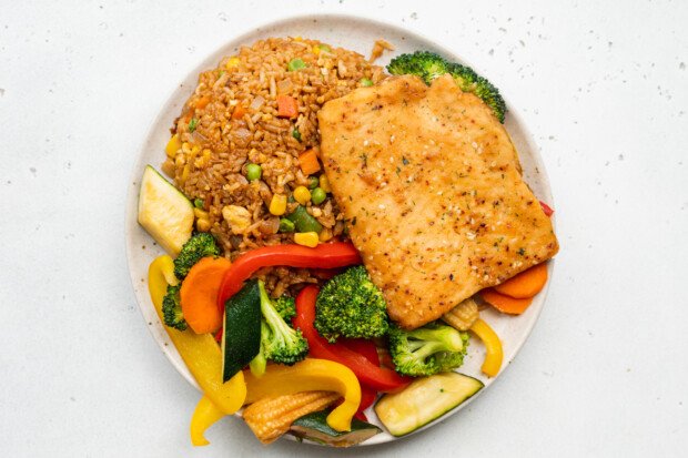 Overhead view of teriyaki sesame salmon fillets, hibachi fried rice, and sautéed vegetables on a plate.