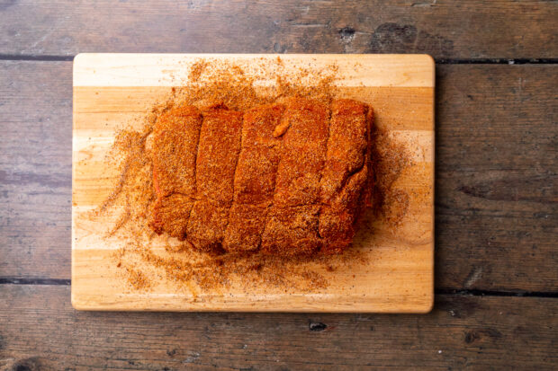 Overhead view of uncooked beef roast covered in taco seasoning on a wooden cutting board.