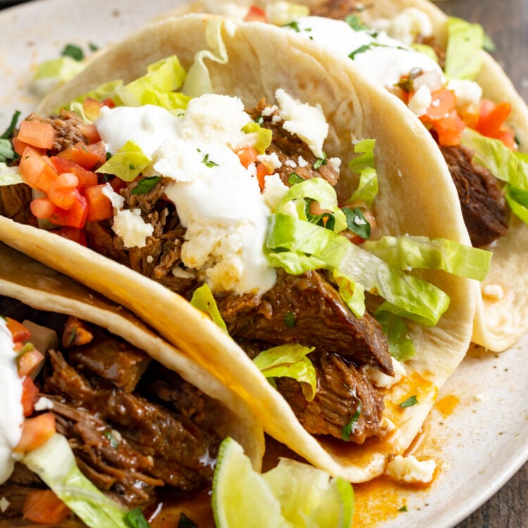 Close-up of shredded beef tacos on a plate surrounded by toppings.