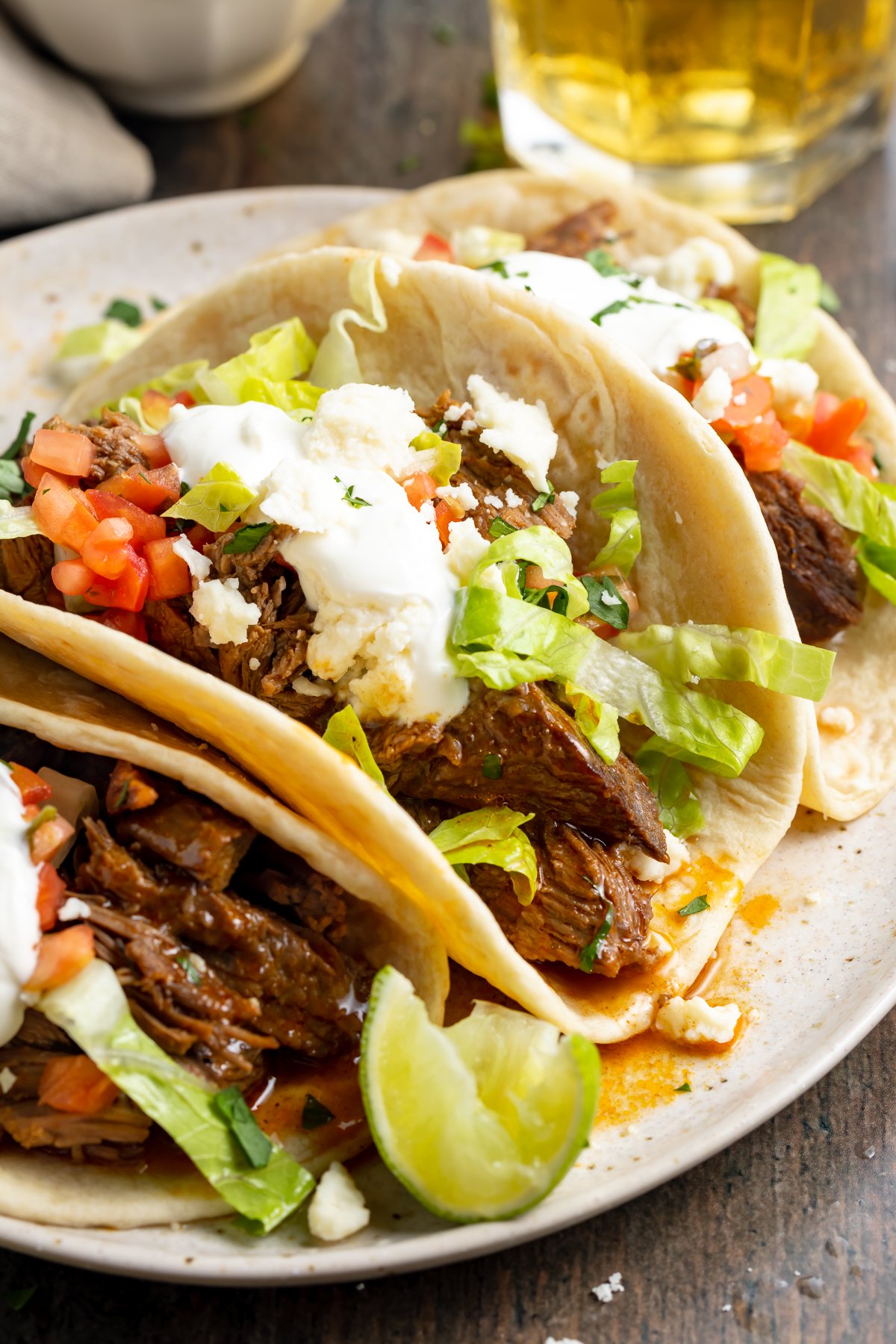 Close-up of shredded beef tacos on a plate surrounded by toppings.