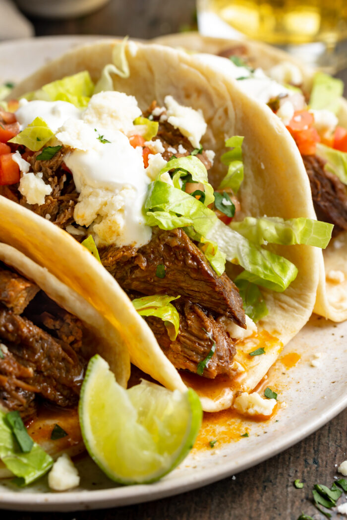 Close-up of shredded beef tacos on a plate surrounded by toppings.