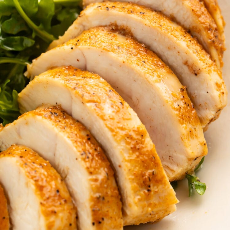 A juicy, Instant Pot chicken breast on a plate with a small salad. The chicken is sliced into 7 slices.