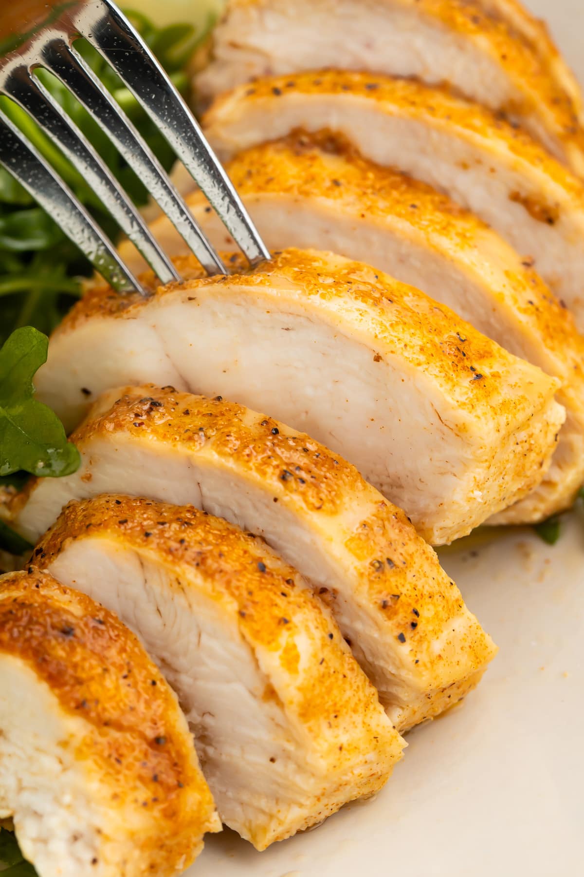 A fork pierces and lifts a slice of an Instant Pot chicken breast off a plate away from other slices of chicken.