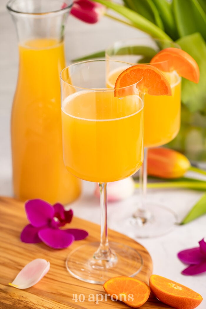 Overhead, angled view of POG juice mimosas in two wine glasses with a carafe of juice in the background.