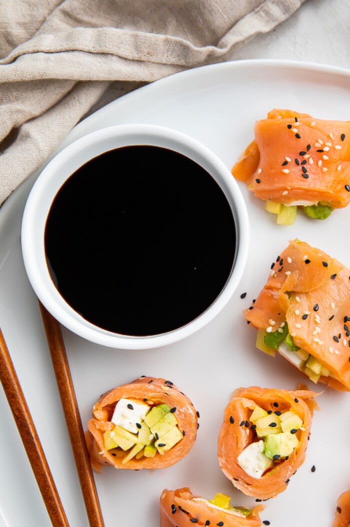 Overhead view of a bowl of soy sauce on a plate with smoked salmon sushi.