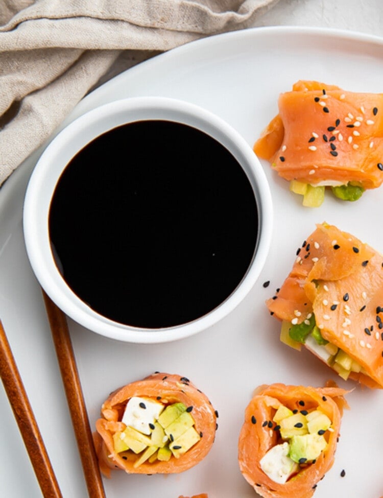 Overhead view of a bowl of soy sauce on a plate with smoked salmon sushi.