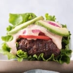 Side view of a Whole30 burger with spicy mayo wrapped in lettuce with tomatoes and red onion.