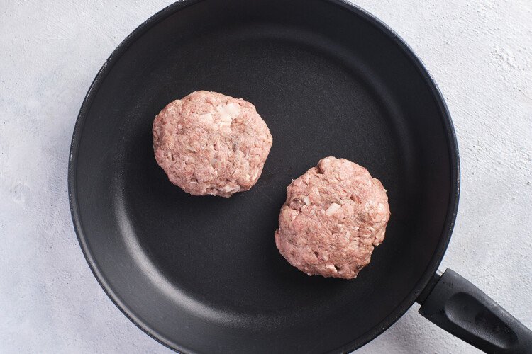Overhead view of 2 Whole30 burger patties in a large cast iron skillet.