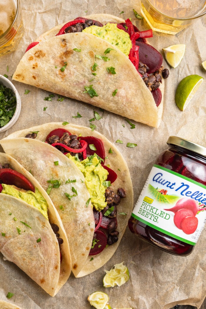 Overhead view of 3 pickled beet tacos on parchment paper with a jar of pickled beets