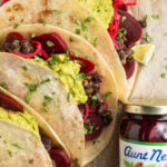 Close-up view of 3 pickled beet tacos topped with guacamole next to a jar of pickled beets.